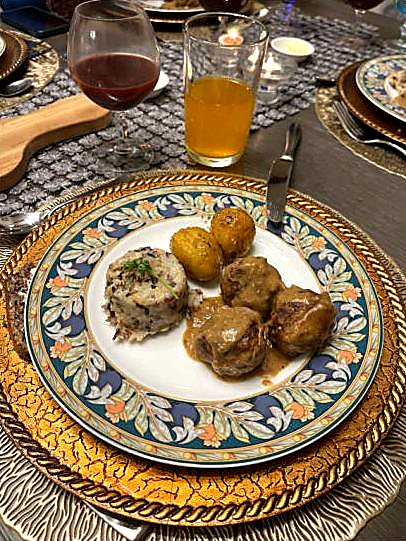 Swedish meatballs in gravy with roasted potatoes on a patterned plate.