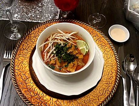 A bowl of laksa with bean sprouts, herbs, and a lime wedge on a gold charger.